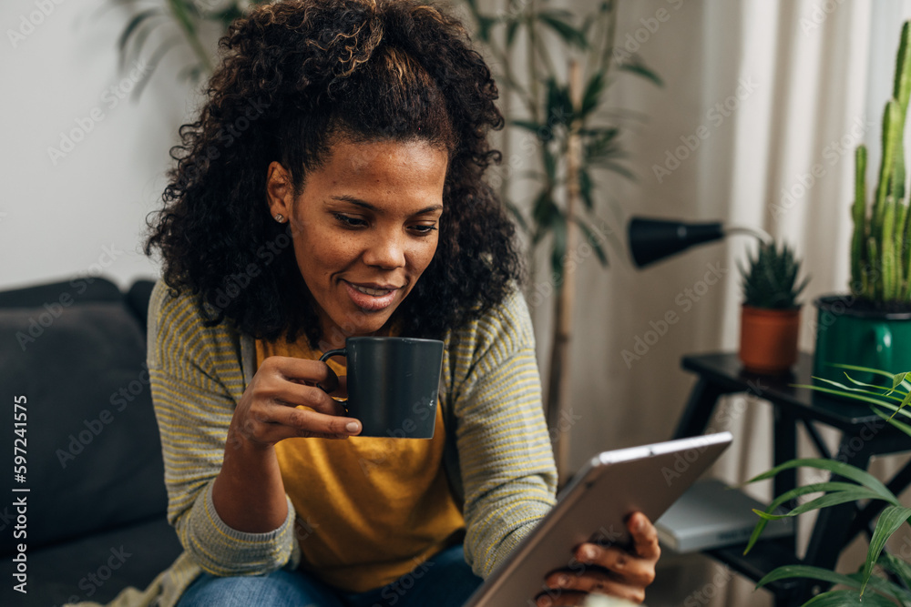 A beautiful multiracial woman is sitting on the sofa and using digital tablet. A beautiful multiracial woman is sitting on the sofa and using digital tablet.