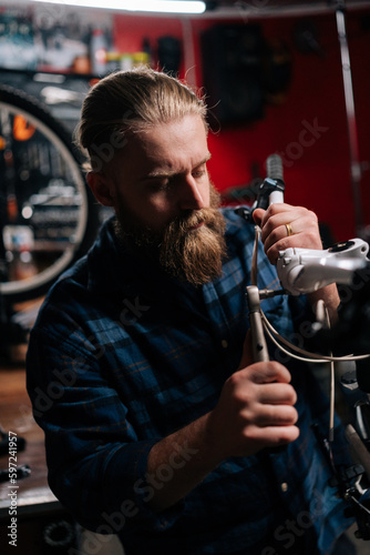 Vertical portrait of handsome bearded repairman checking and repairing bicycle handlebar with special tools working in bike repair shop with dark interior. Concept of professional maintenance of bike.