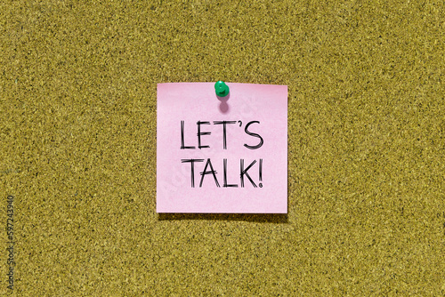 Let's talk text on pink post-it paper pinned on bulletin cork board. This message can be used in business concept about talking together. photo