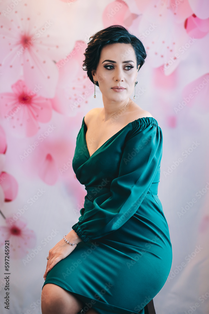 Spring style studio portrait of luxurious lady sitting on the chair in front of the pink flower background