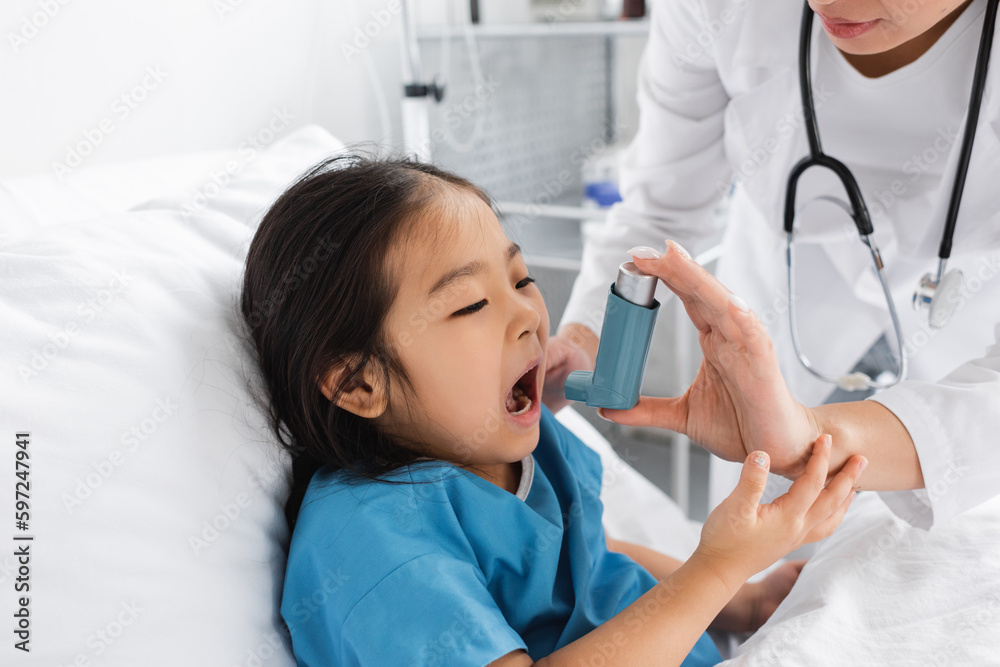 asian girl opening mouth near doctor using inhaler in pediatric clinic. asian girl opening mouth near doctor using inhaler in pediatric clinic.