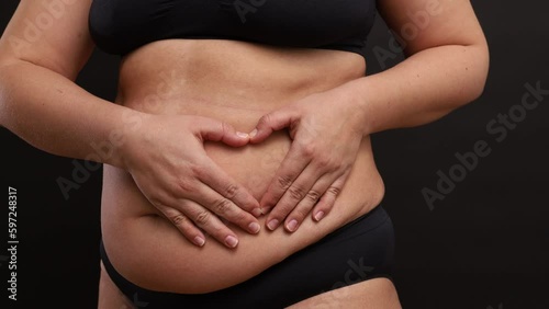 Wallpaper Mural Side view of unrecognizable overweight woman wearing black sportswear, standing on black background, making heart sign with hands fingers on naked belly, gesturing. Health, body positive, self-love. Torontodigital.ca