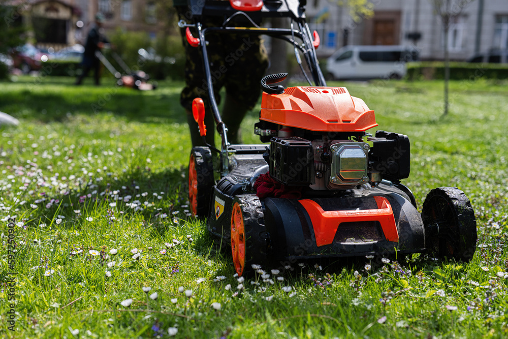 Communal services gardener worker man using lawn mower for grass cutting in city park. Communal services gardener worker man using lawn mower for grass cutting in city park.