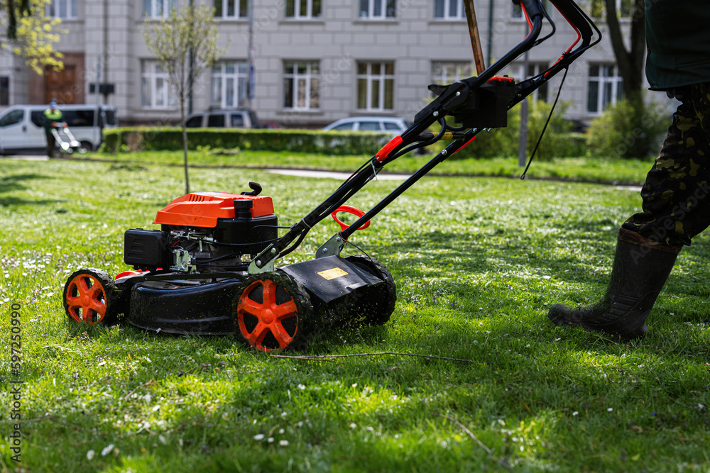 Communal services gardener worker man using lawn mower for grass cutting in city park. Communal services gardener worker man using lawn mower for grass cutting in city park.