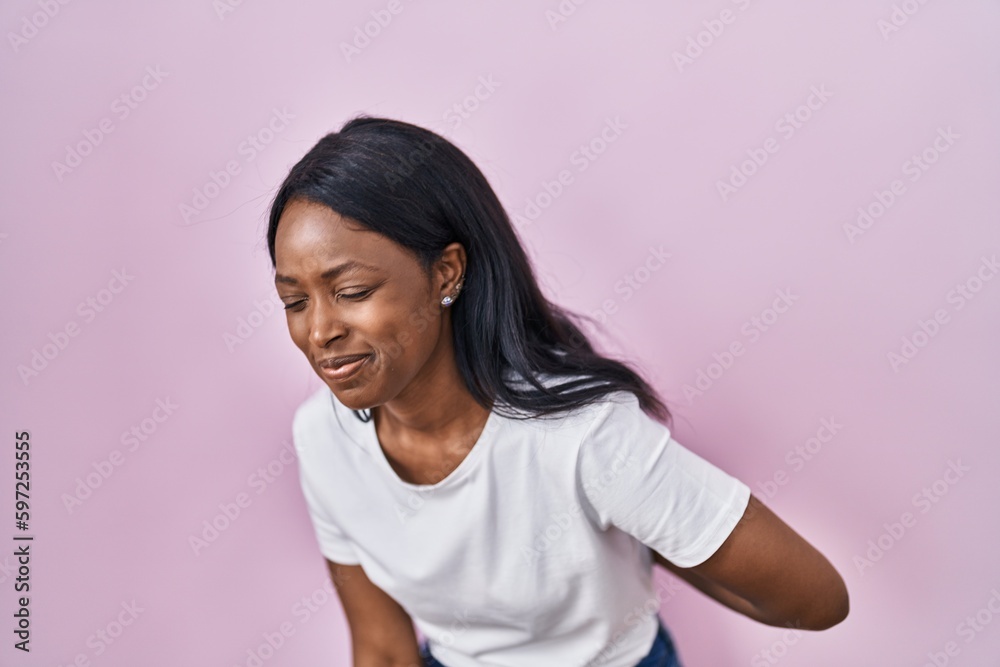 African young woman wearing casual white t shirt suffering of backache, touching back with hand, muscular pain African young woman wearing casual white t shirt suffering of backache, touching back with hand, muscular pain