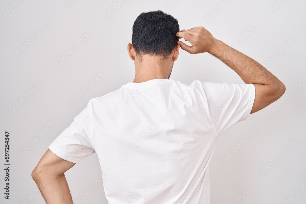 Handsome hispanic man standing over white background backwards thinking about doubt with hand on head Handsome hispanic man standing over white background backwards thinking about doubt with hand on head