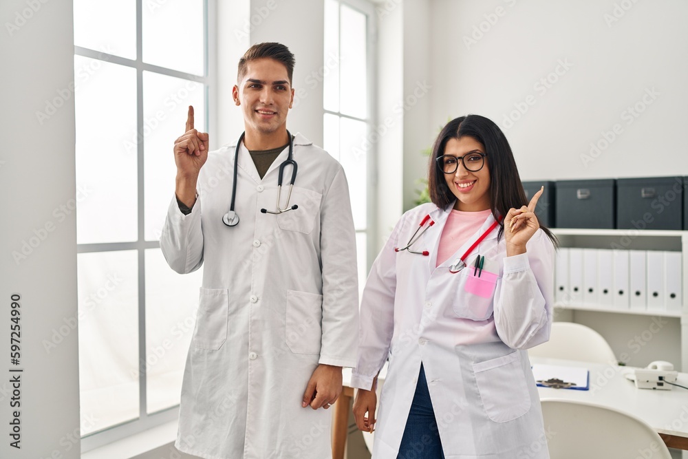 Young doctors wearing uniform and stethoscope at the clinic smiling with an idea or question pointing finger up with happy face, number one Young doctors wearing uniform and stethoscope at the clinic smiling with an idea or question pointing finger up with happy face, number one
