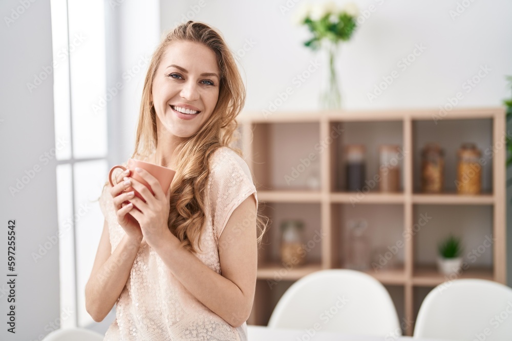 Young blonde woman smiling confident drinking coffee at home