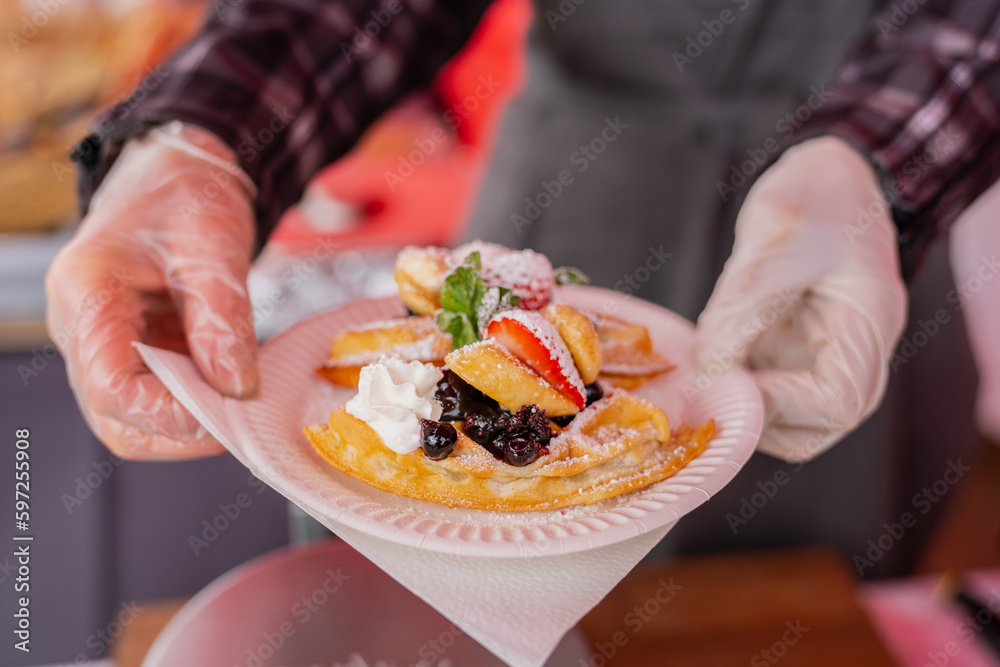 Woman chef cafeteria holding fresh waffles with whipped cream and fresh fruits with powdered sugar at festival