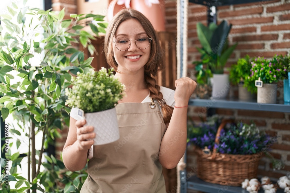 Young caucasian woman working at florist shop holding plant screaming proud, celebrating victory and success very excited with raised arm Young caucasian woman working at florist shop holding plant screaming proud, celebrating victory and success very excited with raised arm