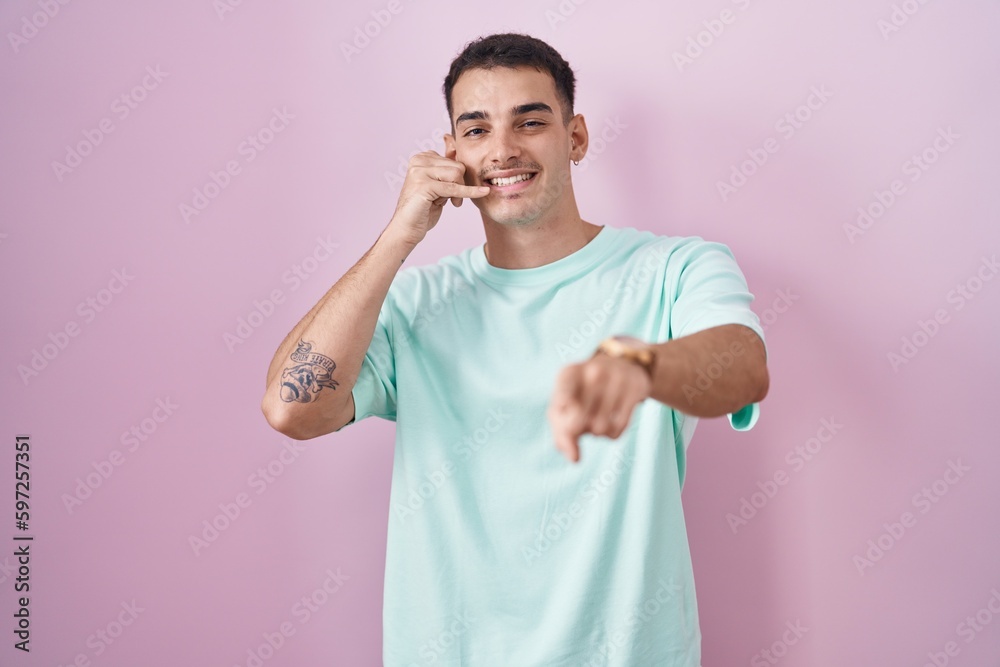 Handsome hispanic man standing over pink background smiling doing talking on the telephone gesture and pointing to you. call me. Handsome hispanic man standing over pink background smiling doing talking on the telephone gesture and pointing to you. call me.