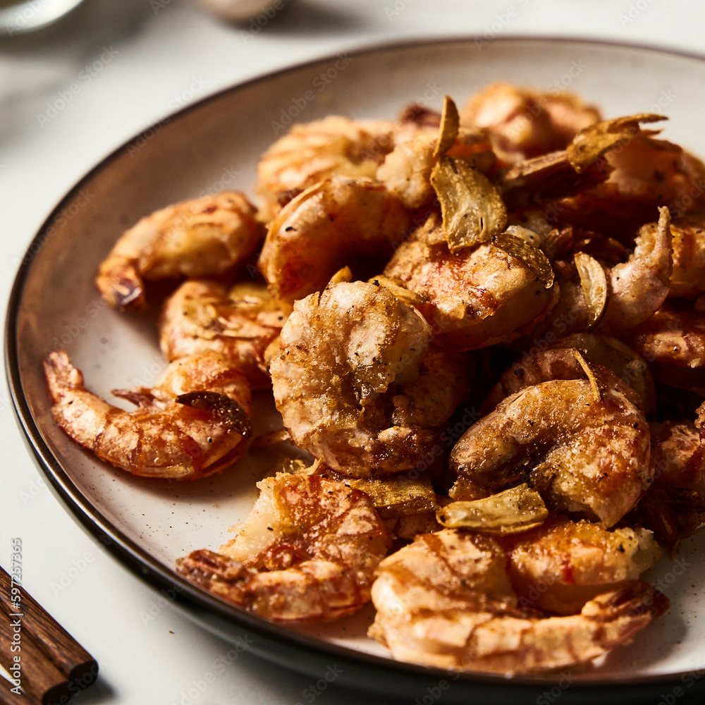 Crispy Pan fried tiger shrimps or prawns with garlic. Chinese or Asian cuisine dish. Shrimps lay on white plate on white marble background. Close up food