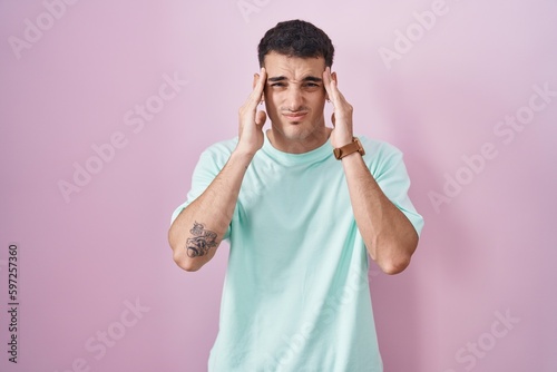 Handsome hispanic man standing over pink background with hand on head, headache because stress. suffering migraine.