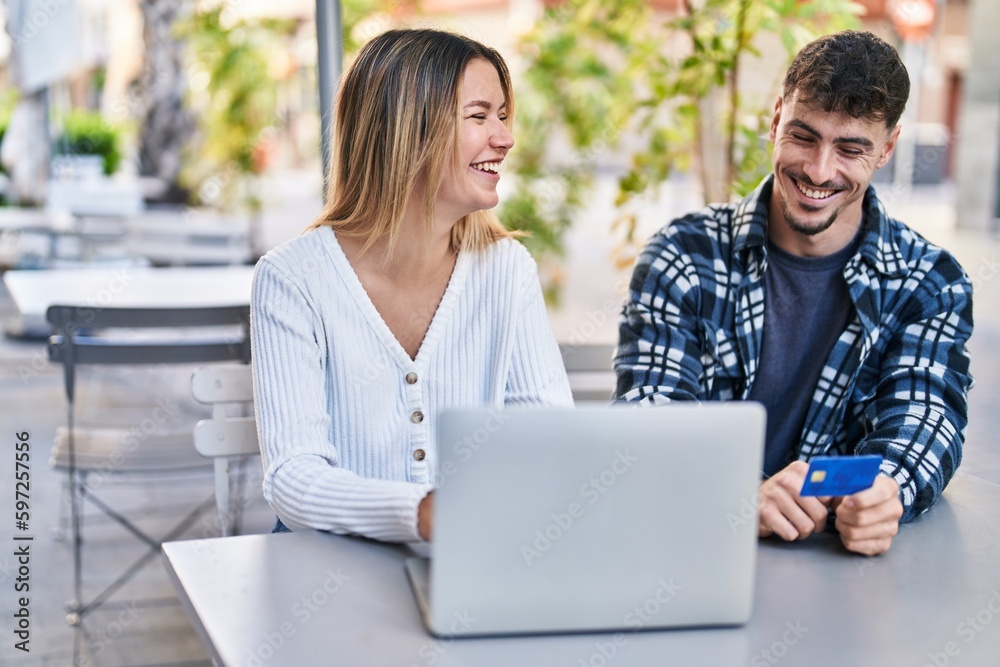 Young man and woman couple using laptop and credit card sitting on table at coffee shop terrace Young man and woman couple using laptop and credit card sitting on table at coffee shop terrace