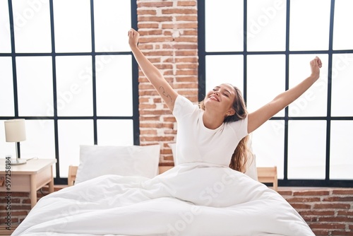 Young beautiful hispanic woman waking up stretching arms at bedroom