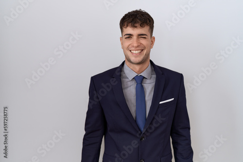 Young hispanic business man wearing suit and tie winking looking at the camera with sexy expression, cheerful and happy face.