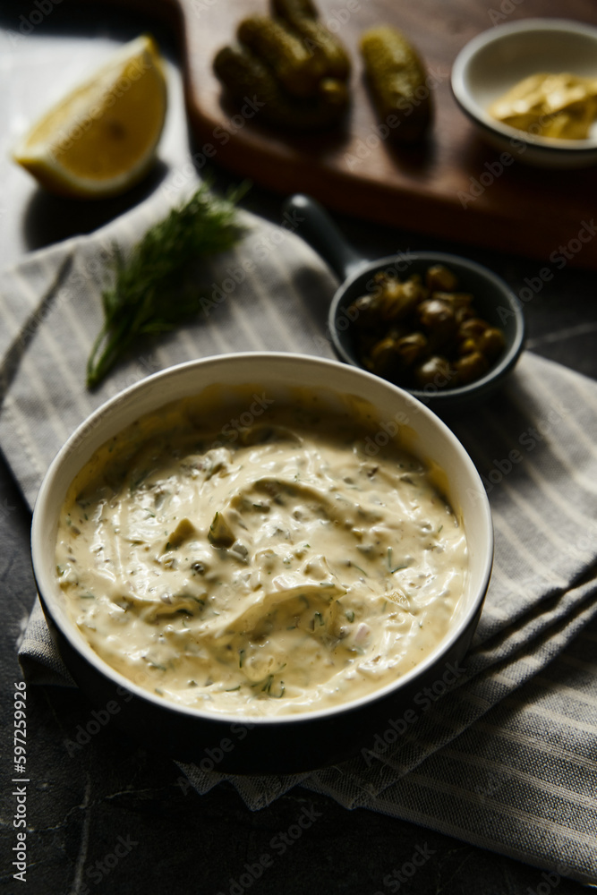 Classic Tartar Sauce with it ingredients on dark stone or marble background. Mayonnaise with dill and pickled cucumbers with lemon. Classic Tartar Sauce with it ingredients on dark stone or marble background. Mayonnaise with dill and pickled cucumbers with lemon.