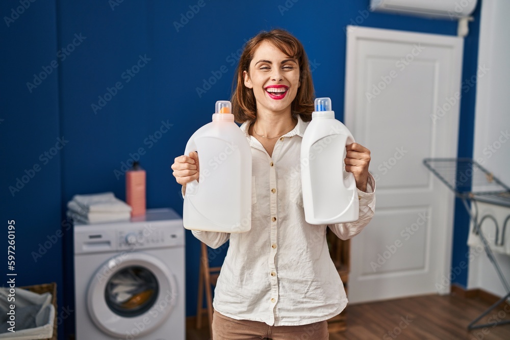 Young beautiful woman holding detergent bottles smiling with a happy and cool smile on face. showing teeth. Young beautiful woman holding detergent bottles smiling with a happy and cool smile on face. showing teeth.