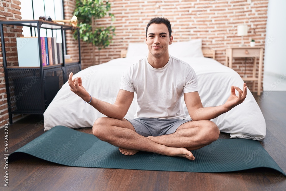 Fototapeta premium Young hispanic man doing yoga exercise sitting on floor at bedroom