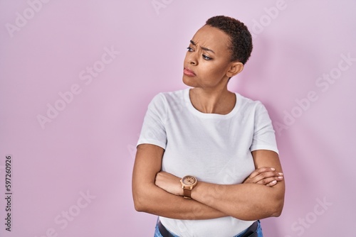 Beautiful african american woman standing over pink background looking to the side with arms crossed convinced and confident