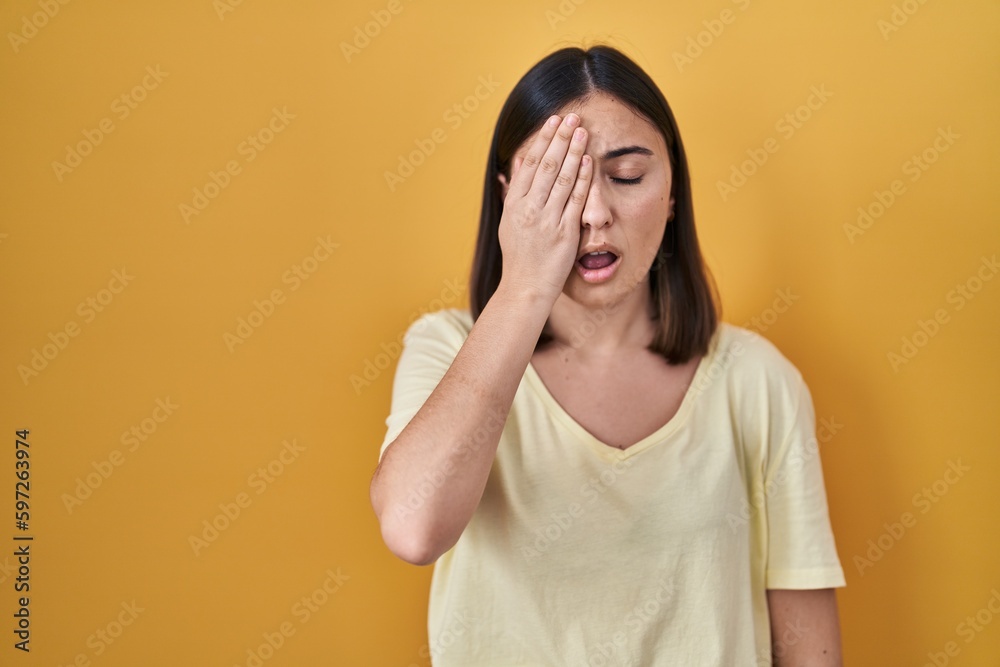 Hispanic girl wearing casual t shirt over yellow background yawning tired covering half face, eye and mouth with hand. face hurts in pain. Hispanic girl wearing casual t shirt over yellow background yawning tired covering half face, eye and mouth with hand. face hurts in pain.