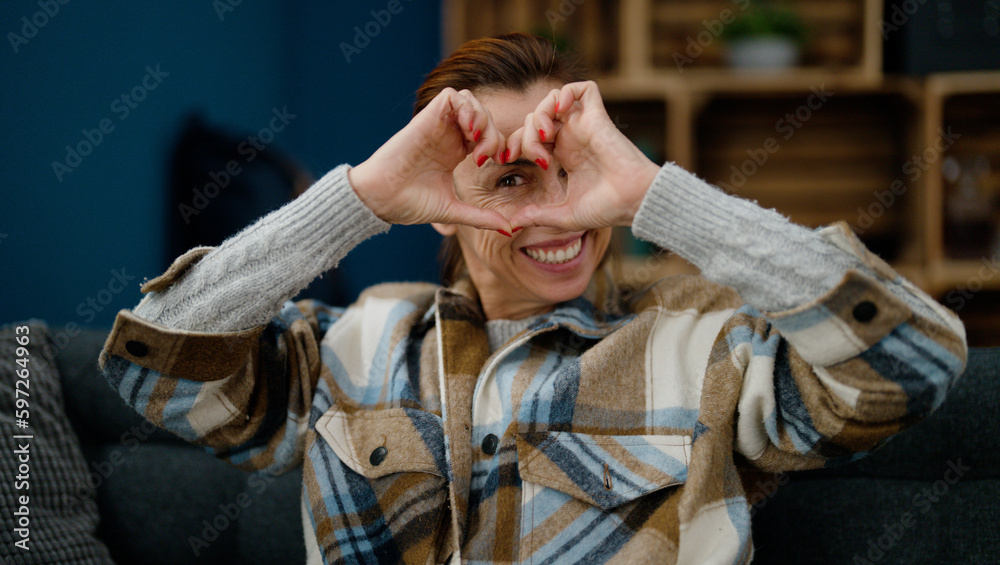 Obraz premium Middle age hispanic woman doing heart symbol with hands sitting on sofa at home