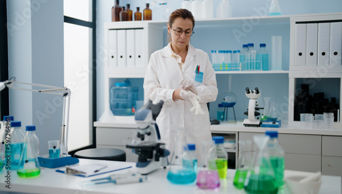 Middle age hispanic woman wearing scientist uniform and gloves at laboratory