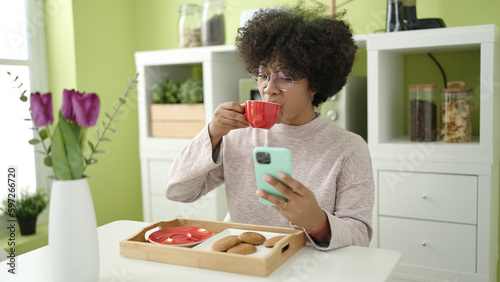 Young african american woman having breakfast using smartphone at home
