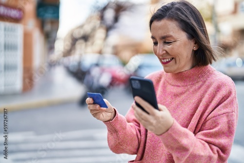 Middle age woman using smartphone and credit card at street