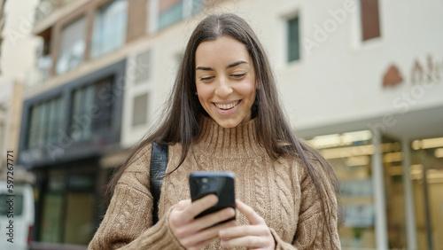 Young beautiful hispanic woman using smartphone smiling at street