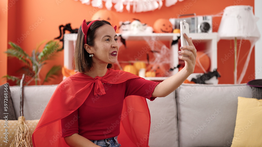 Young beautiful hispanic woman wearing devil costume make selfie by smartphone at home