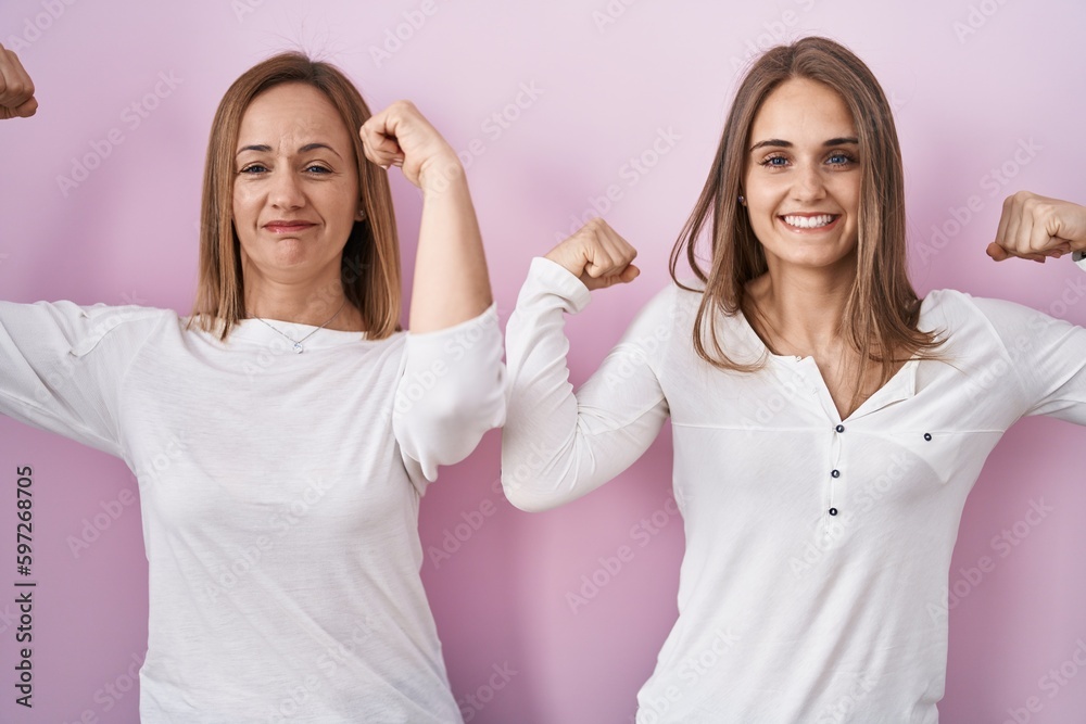 Middle age mother and young daughter standing over pink background showing arms muscles smiling proud. fitness concept. Middle age mother and young daughter standing over pink background showing arms muscles smiling proud. fitness concept.