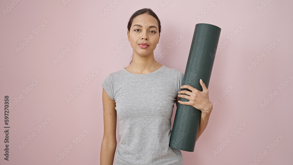 Young beautiful hispanic woman wearing sportswear holding yoga mat over isolated pink background Young beautiful hispanic woman wearing sportswear holding yoga mat over isolated pink background