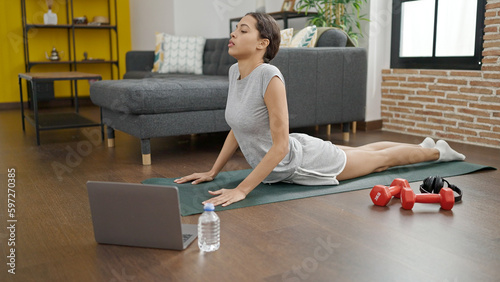 Young beautiful hispanic woman doing yoga with laptop at home