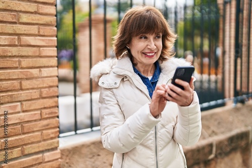 Middle age woman smiling confident using smartphone at street