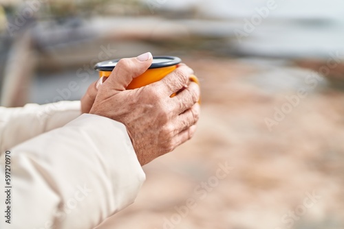Middle age woman holding cup of coffee at seaside