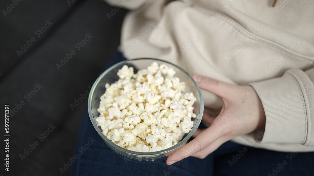 Young blonde woman sitting on sofa eating popcorn at home Young blonde woman sitting on sofa eating popcorn at home
