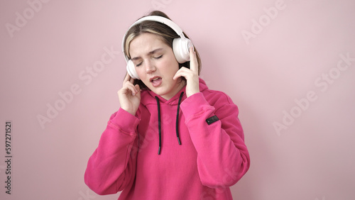 Young blonde woman listening to music over isolated pink background