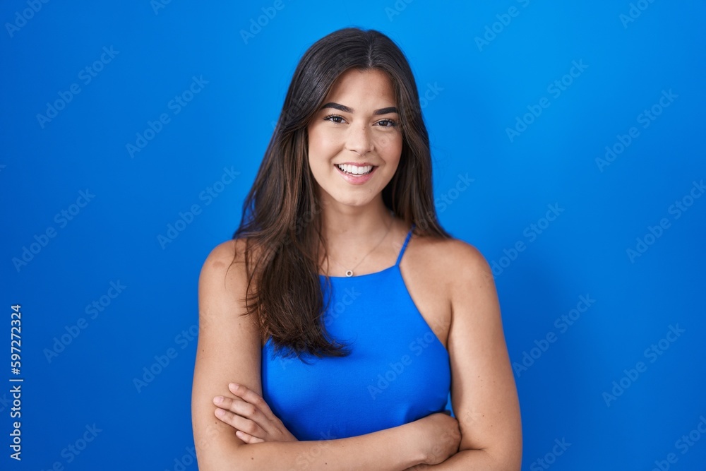 Hispanic woman standing over blue background happy face smiling with crossed arms looking at the camera. positive person. Hispanic woman standing over blue background happy face smiling with crossed arms looking at the camera. positive person.