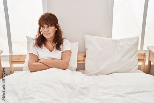 Middle age woman sitting on bed with worried expression at bedroom