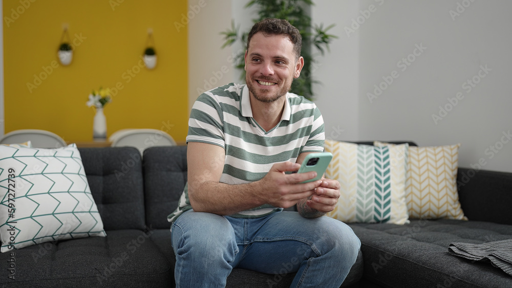 Young caucasian man smiling using smartphone sitting on the sofa at home Young caucasian man smiling using smartphone sitting on the sofa at home