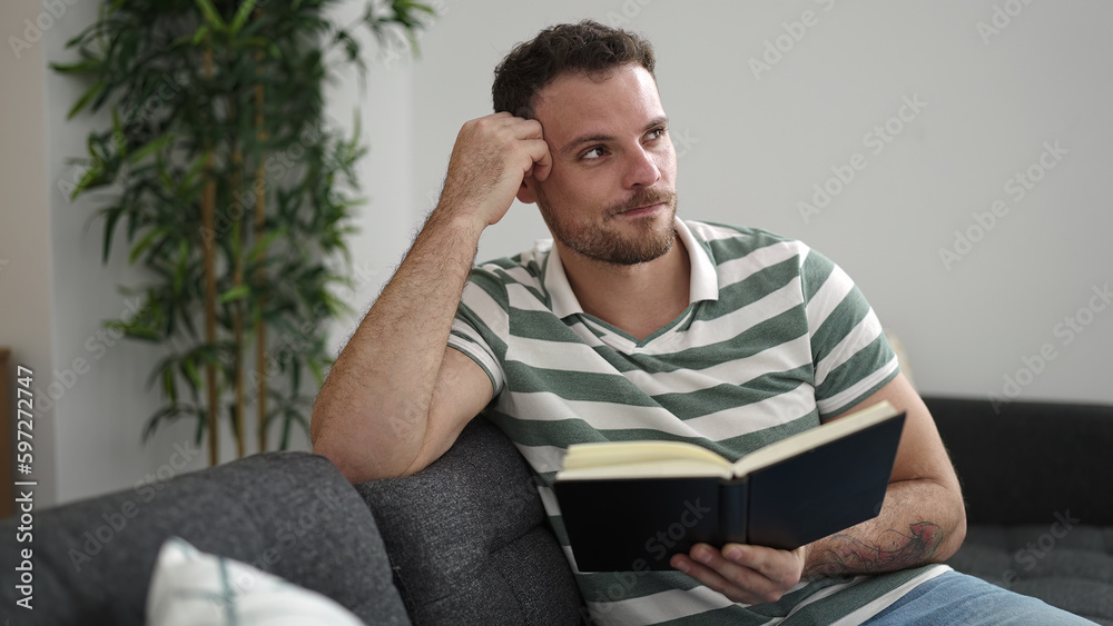 Young caucasian man reading a book sitting on the sofa at home Young caucasian man reading a book sitting on the sofa at home