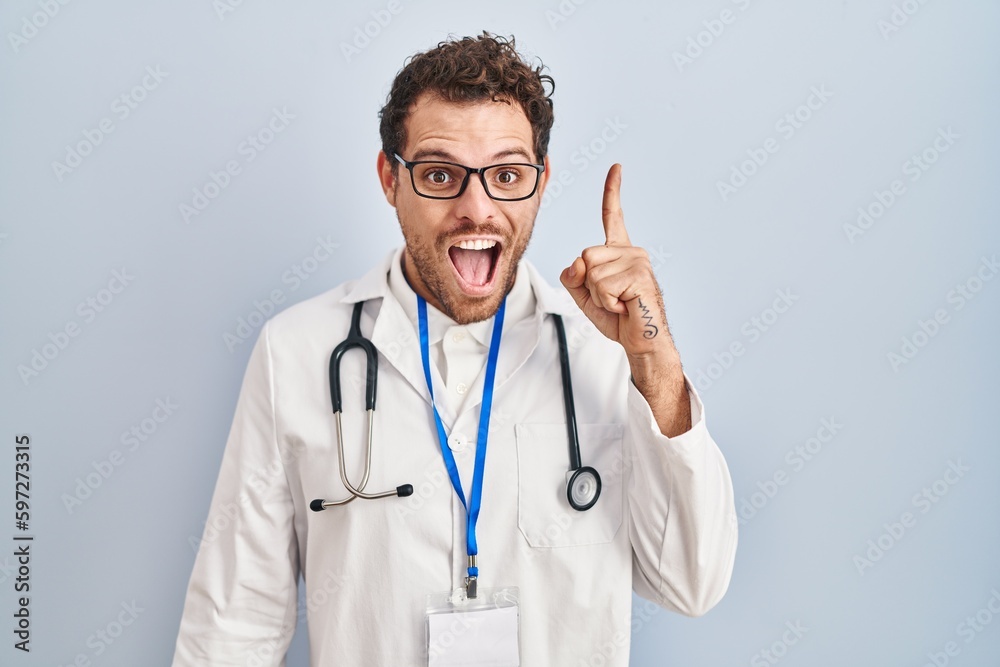Young hispanic man wearing doctor uniform and stethoscope pointing finger up with successful idea. exited and happy. number one. Young hispanic man wearing doctor uniform and stethoscope pointing finger up with successful idea. exited and happy. number one.