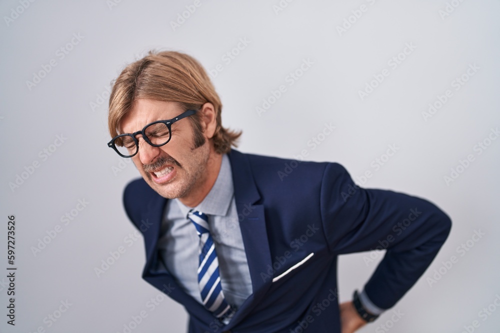 Caucasian man with mustache wearing business clothes suffering of backache, touching back with hand, muscular pain Caucasian man with mustache wearing business clothes suffering of backache, touching back with hand, muscular pain