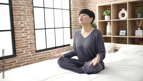 Young chinese woman doing yoga exercise sitting on bed at bedroom