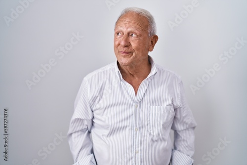 Senior man with grey hair standing over isolated background smiling looking to the side and staring away thinking.