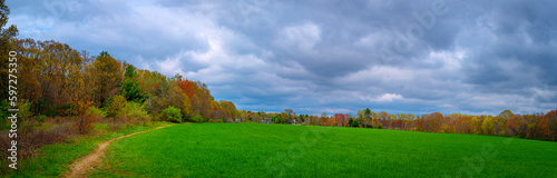 Green agricultural field surrounded by the colorful trees on a dramatic cloudy day in the spring in New England, USA
