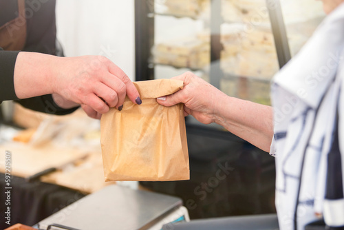 Buy sweets in a confectionery shop. The woman takes a bag of sweet biscuits from the seller and pays him. Hands of the seller and the buyer with money close-up