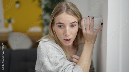 Tableau sur toile Young blonde woman listening through wall with glass at home