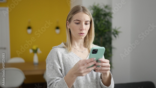 Young blonde woman using smartphone at home